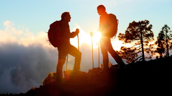 Untitled design (21) a couple of men standing on top of a mountain